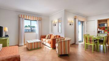 Una sala de estar con sofá, sillones, una mesa de centro y televisor. Hay un comedor con mesa y sillas.