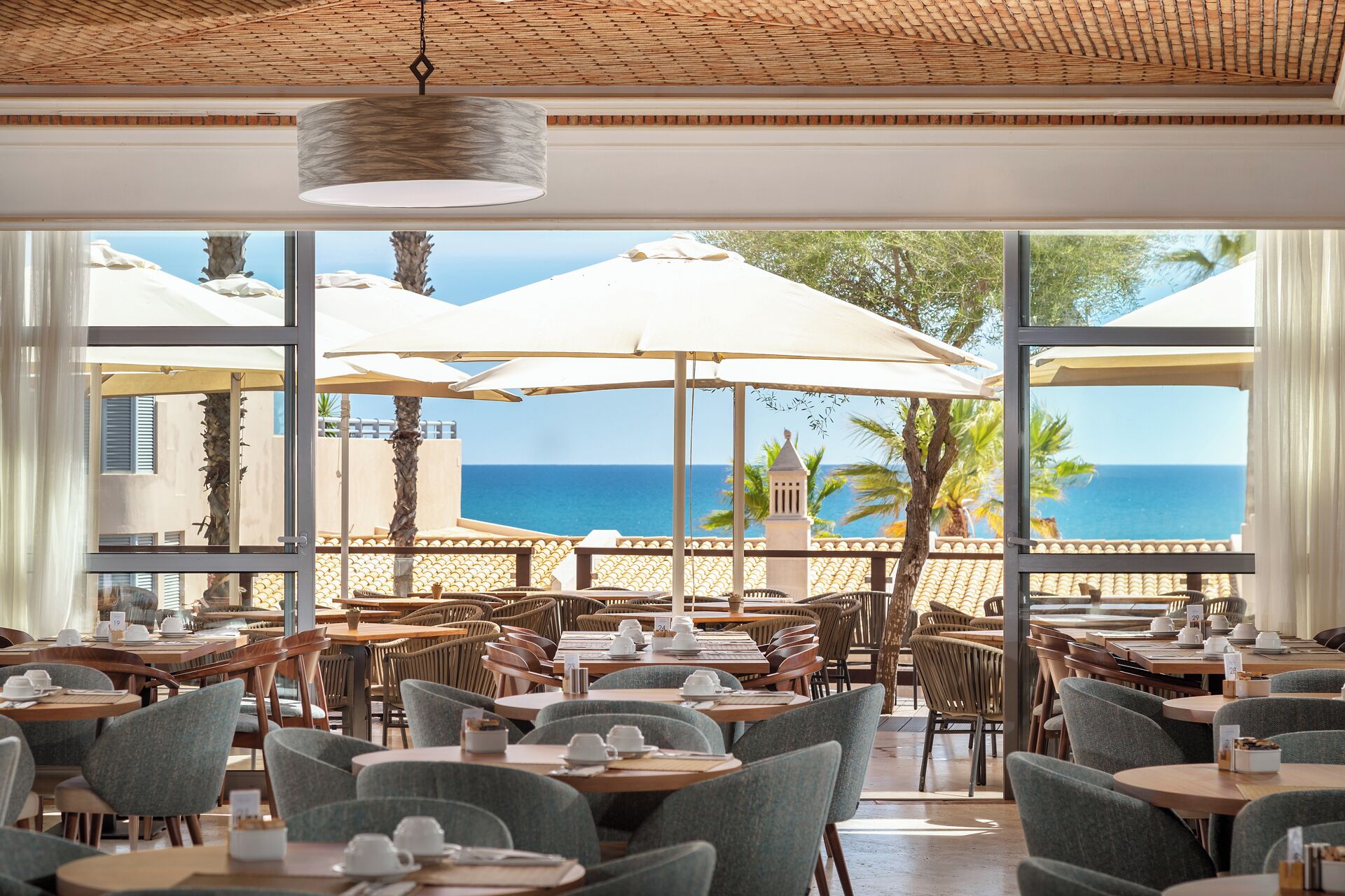 A restaurant with outdoor seating overlooking the sea, featuring wicker furniture and umbrellas.