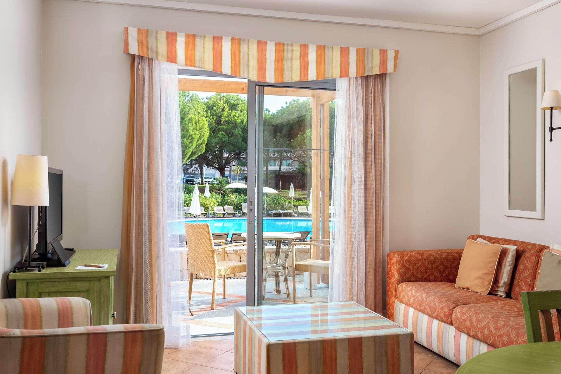 Habitación con puerta de vidrio que da a un área de piscina al aire libre, un sofá, un escritorio con lámpara y una silla.