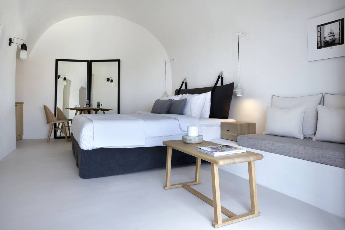 Ein modernes Schlafzimmer mit Bett, Nachttisch, Lampe, Stuhl und einem großen Spiegel.