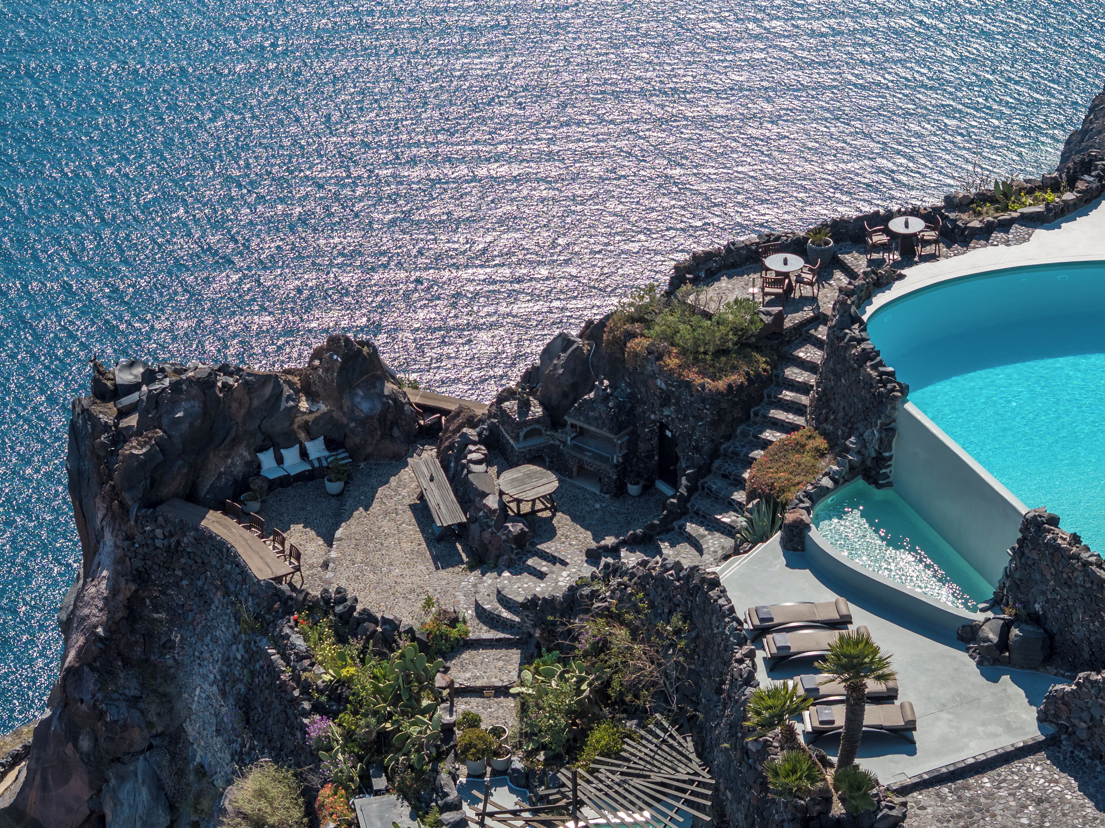 A coastal resort with a pool, outdoor seating, and a rocky landscape.