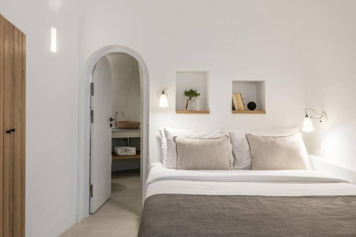 Un dormitorio con cama, un armario de madera, una pared blanca con estantes y una puerta que da a un baño.