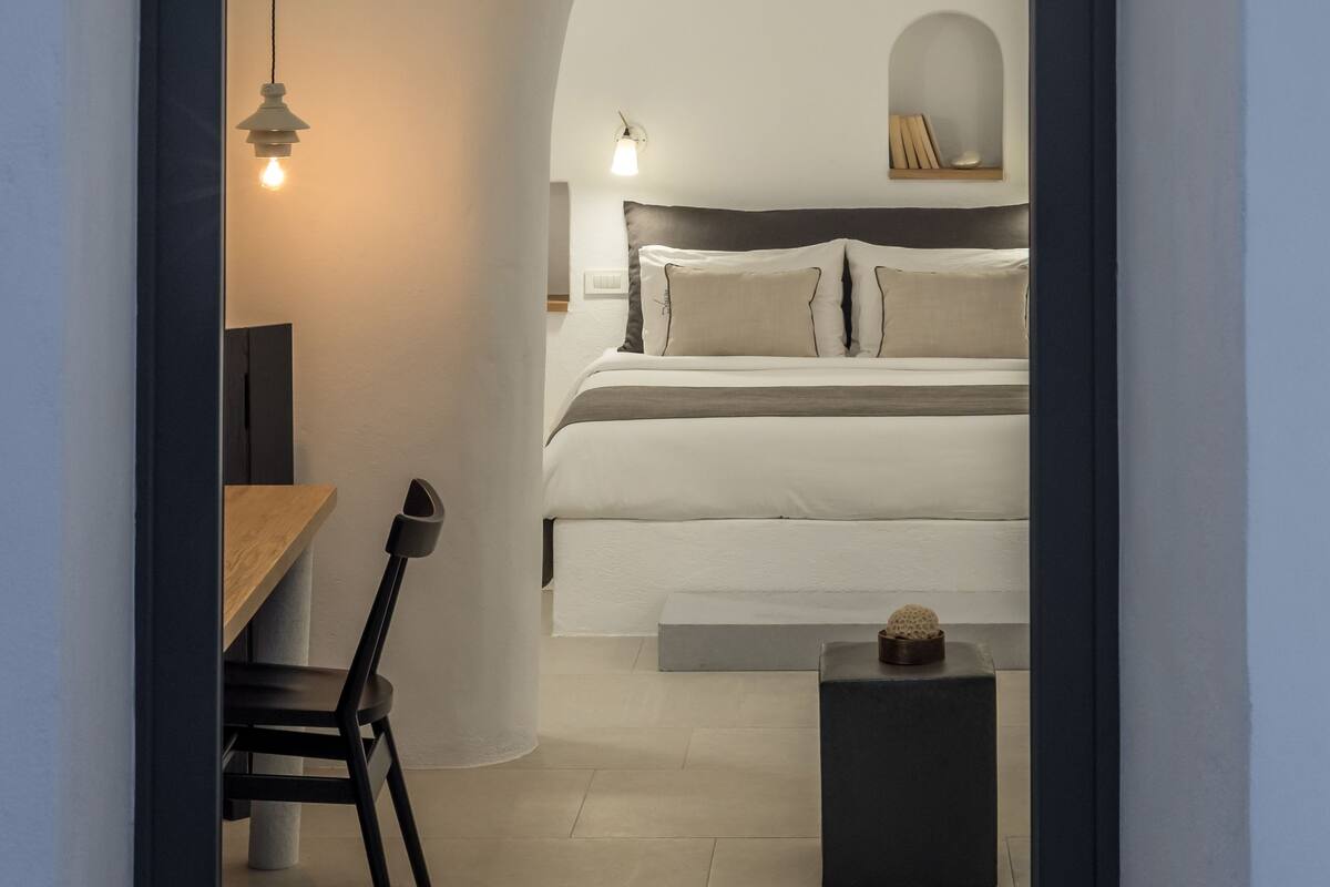 Ein modernes Interieur mit Essbereich, einem Bett mit Kopfteil und einem kleinen Tisch mit Lampe.