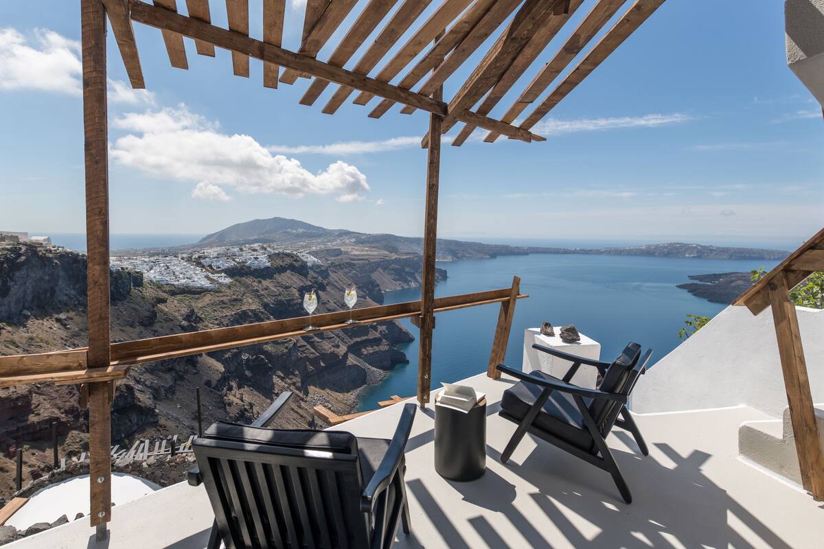 Eine hölzerne Pergola mit Blick auf eine malerische Küstenlandschaft, inklusive Tisch und zwei Stühlen.