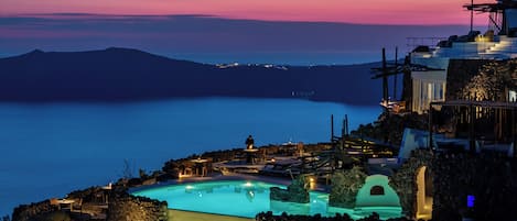 Un lujoso resort frente al mar, con una amplia piscina infinita, arquitectura de piedra y vistas al mar al atardecer.