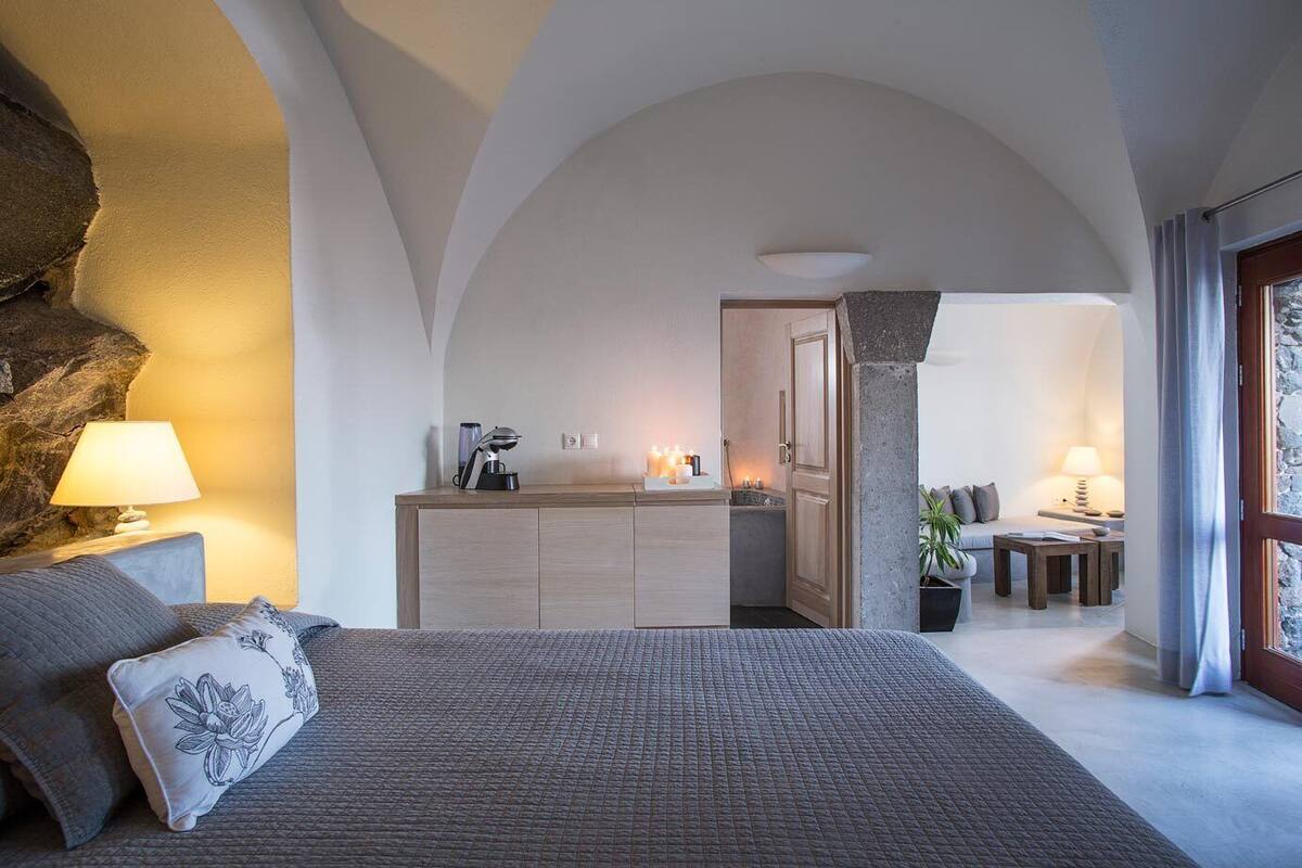 Ein Schlafzimmer mit einem großen Bett, einem Nachttisch, einer Lampe und Blick auf eine Küche sowie ein Wohnbereich.