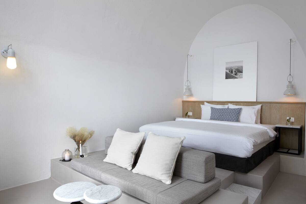 Ein modernes Schlafzimmer mit einem großen Bett, einer Couch und einem kleinen Tisch mit zwei runden weißen Hussen.