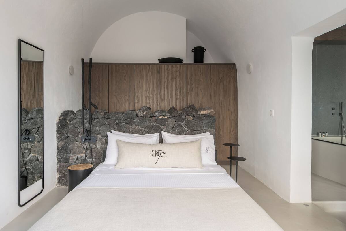 Ein modernes Schlafzimmer mit Steinwand, Holz-Kopfteil und einem Bett mit weißer Bettwäsche.