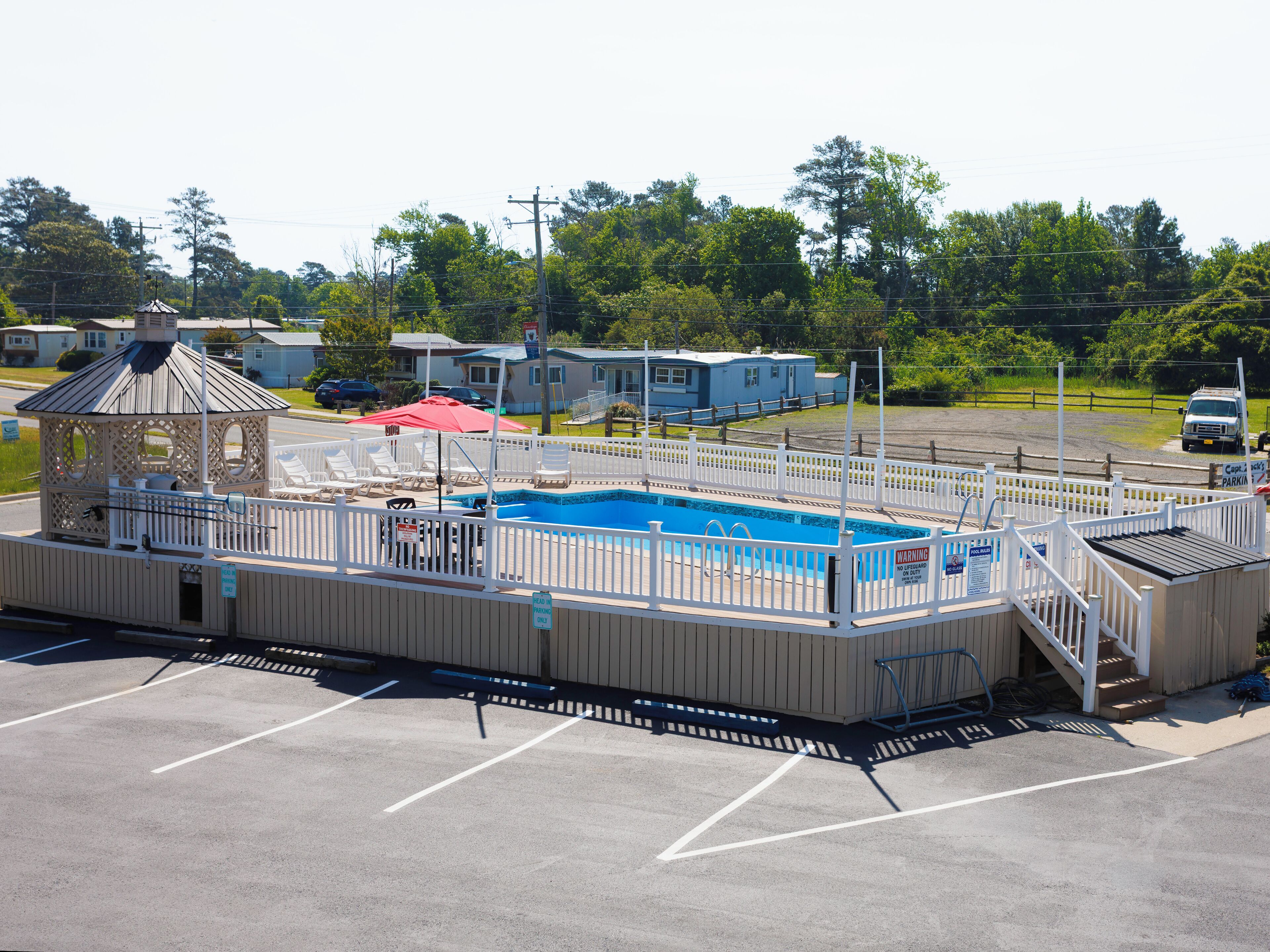Una piscina con un pabellón, una zona de estar cubierta y un estacionamiento.