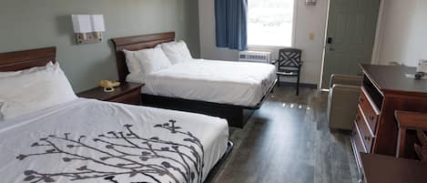 A hotel room with two beds, a desk, a chair, a dresser, a window with curtains, and a door.
