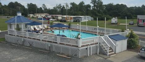 A pool area with a covered deck, lounge chairs, and a gazebo.