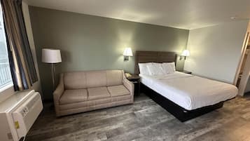 A hotel room with a bed, a sofa, two wall-mounted lamps, and a window with curtains.