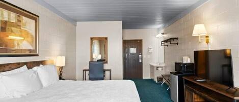 A hotel room with a large bed, a desk with a chair, a television, and a mirror.