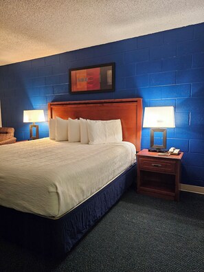 A hotel room with a large bed, two bedside tables with lamps, a wooden headboard, and a blue brick wall.