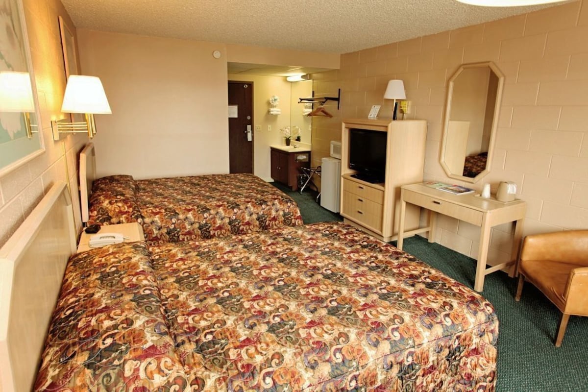 A hotel room with two beds, a desk, a TV, a mirror, and a chair.