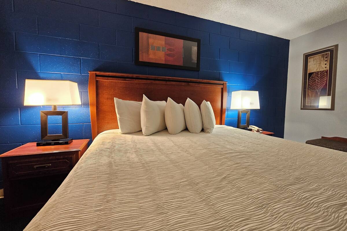 Habitación de hotel con una cama grande, dos mesitas de noche con lámparas, un cabecero de madera y paredes azules.