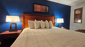 Habitación de hotel con una cama grande, dos mesitas de noche con lámparas, un cabecero de madera y paredes azules.