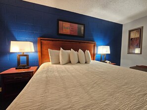 A hotel room with a large bed, two bedside tables with lamps, a wooden headboard, and blue walls.