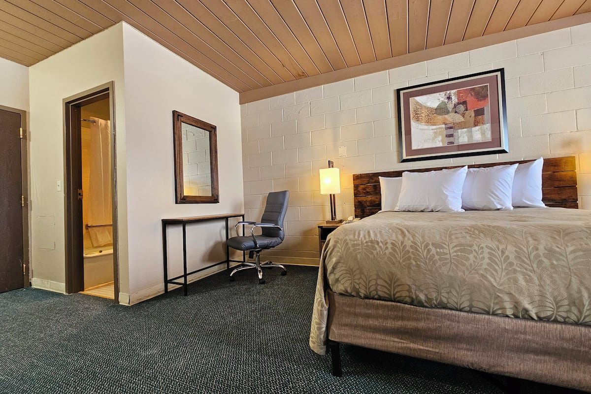 Habitación de hotel con cama, escritorio, silla, lámpara y un cuadro en la pared.