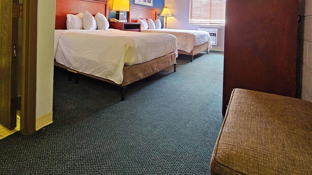 A hotel room with two beds, a wooden wardrobe, a desk, and a window with blinds. - 1st Choice Inn Rawlins (Rawlins)