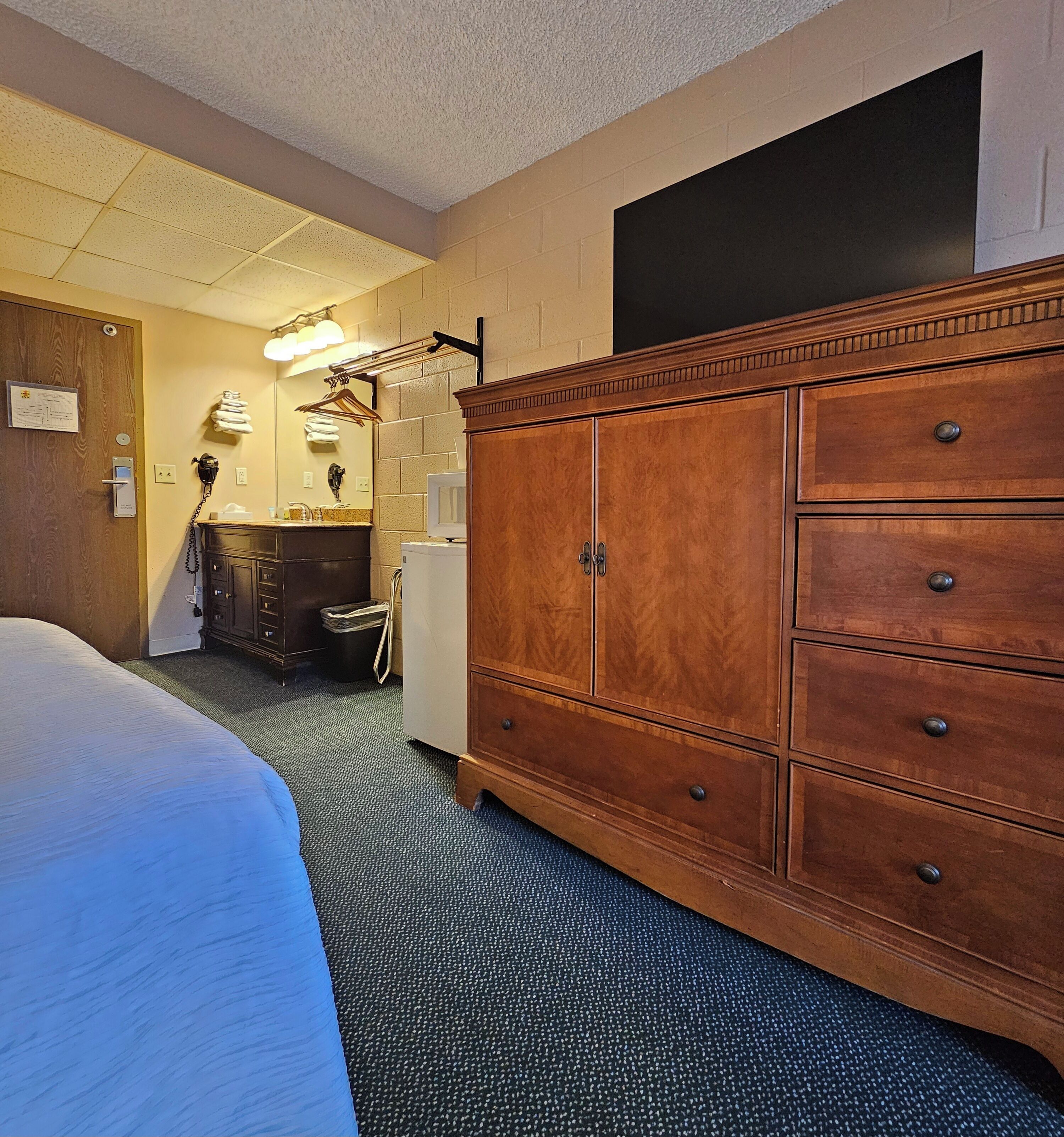 Habitación de hotel con un gran aparador de madera, una cama, un baño con espejo y un perchero para toallas.