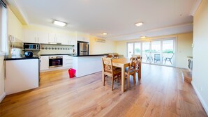 A modern kitchen with white cabinets, a wooden dining table, and a large window providing natural light. - Sunset Island Resort (Surfers Paradise)