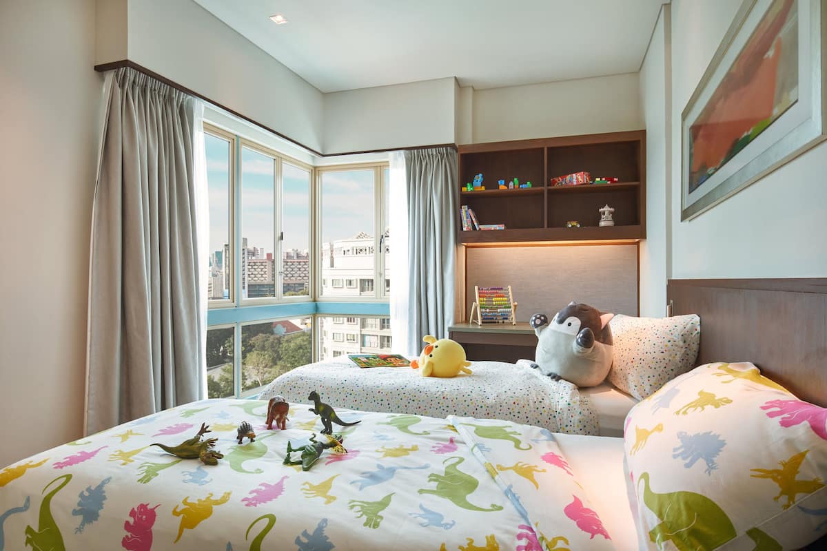 A bedroom with two beds, a window with curtains, a bookshelf, and a city view.