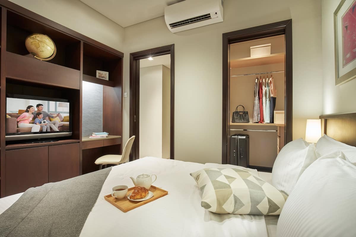 A hotel room with a bed, a television, a desk with a chair, a wardrobe, and a small kitchenette.
