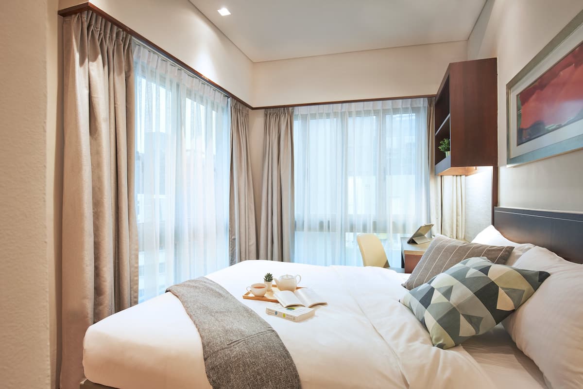 A hotel room with a large bed, a bedside table with a lamp, a chair, and a window with curtains.