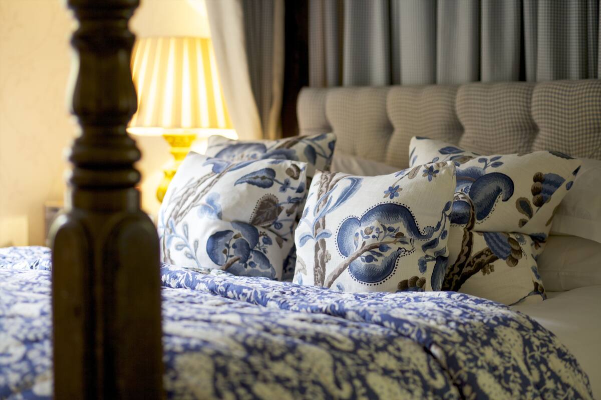 Una cama bien hecha con ropa de cama de diseño azul y blanco, un cabecero de madera y una lámpara en una mesita de noche.
