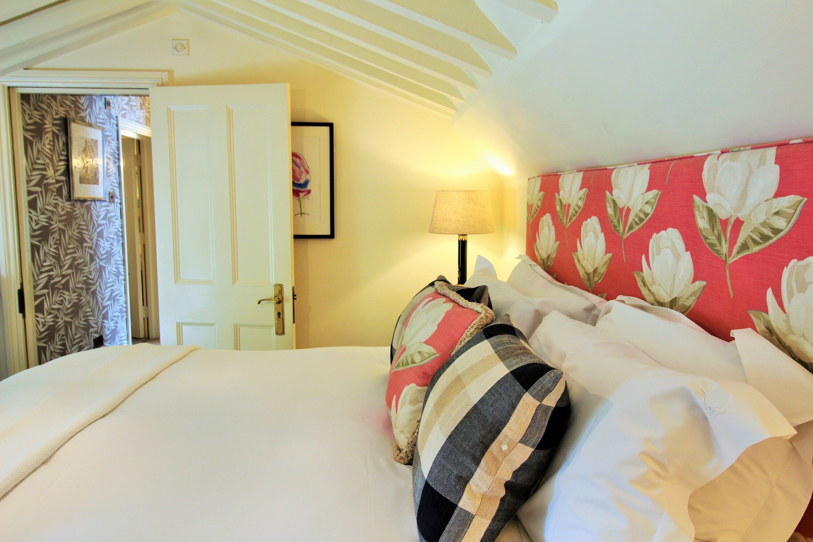 A neatly made bed with white linens and striped pillows, a floral-patterned headboard, and a door with a patterned curtain.