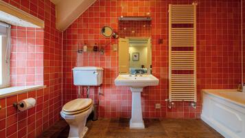 A bathroom with red tiled walls, a white toilet, a pedestal sink, and a wooden towel rack.
