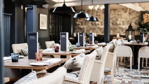 Ein Restaurant mit Korbstühlen, schwarzen Pendelleuchten und einer Steinsäule im Hintergrund.
