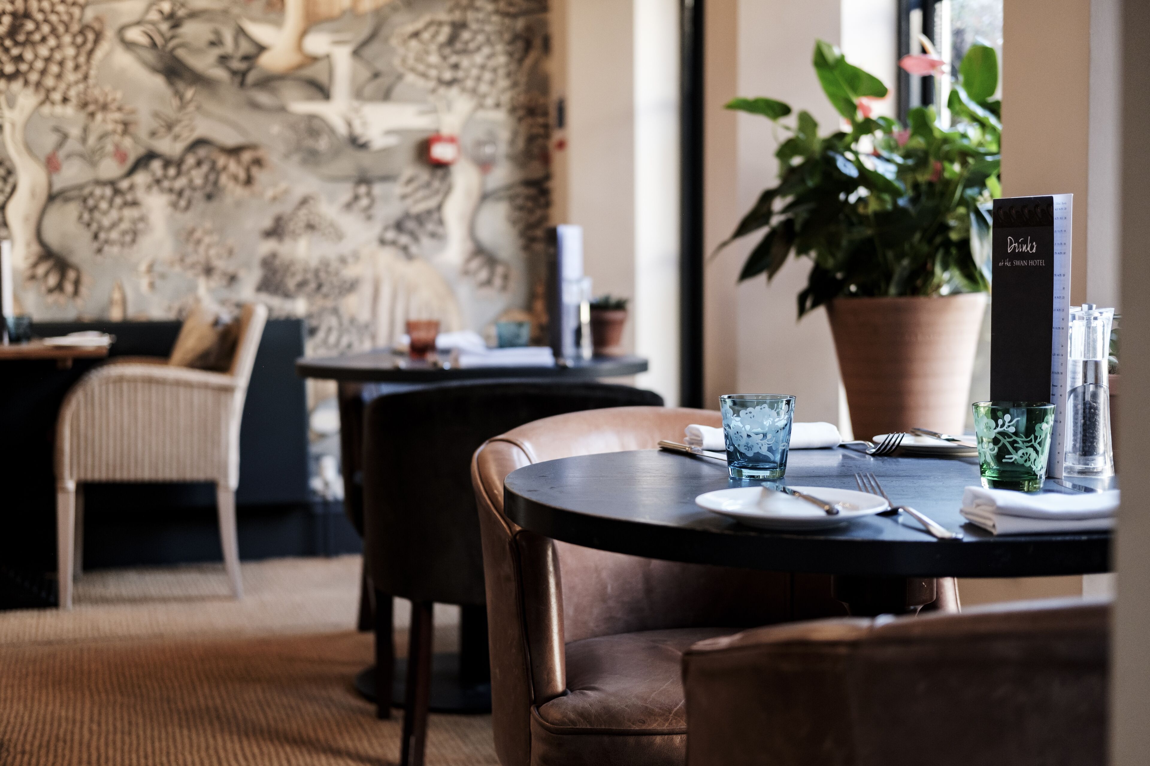 A dining area with a round table set for two, a potted plant, and a menu stand.