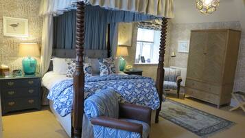 A four-poster canopy bed with a blue and white patterned bedspread, a wooden nightstand with a lamp, a bedside table with a telephone, and a large herringbone-patterned wardrobe.