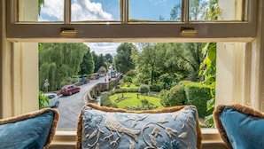 Blick aus einem Fenster mit Kissen, einer Straße und viel Grün.