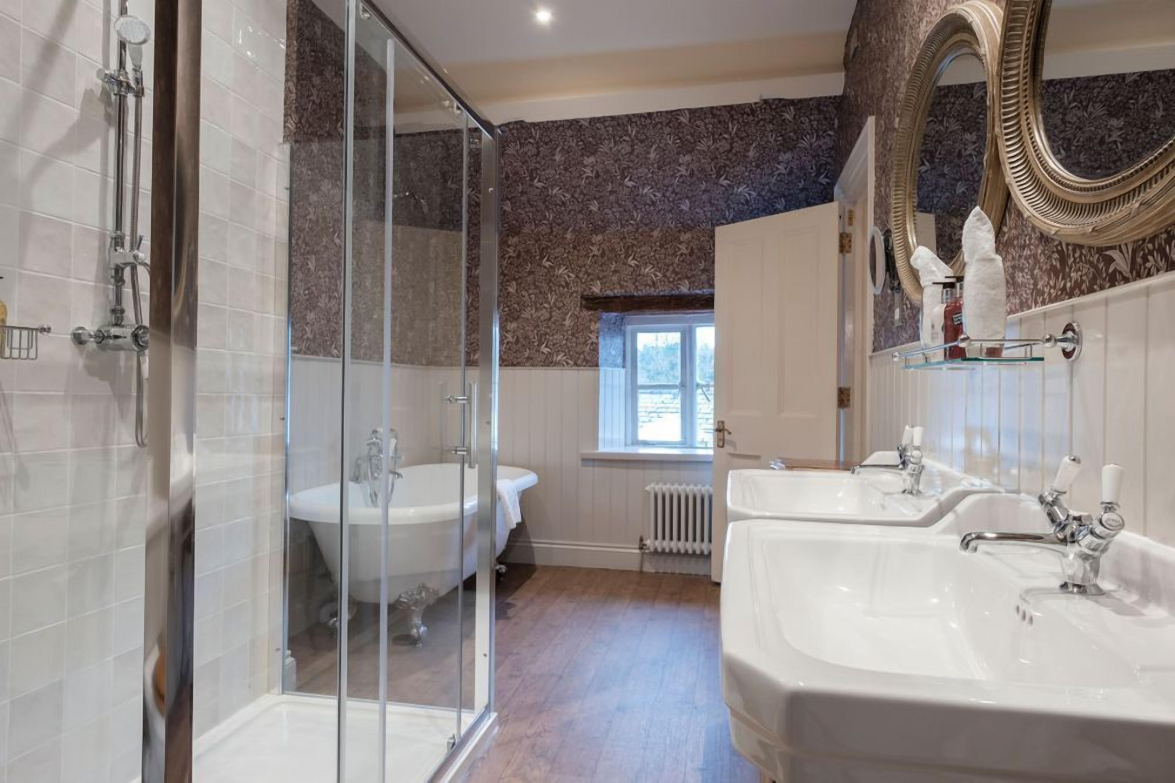 Un baño con cabina de ducha de vidrio, dos lavabos, una bañera y un espejo grande.