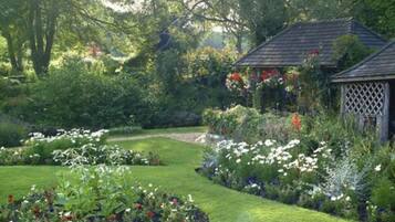 Un jardín con un mirador, abundante vegetación y diversas plantas en flor.