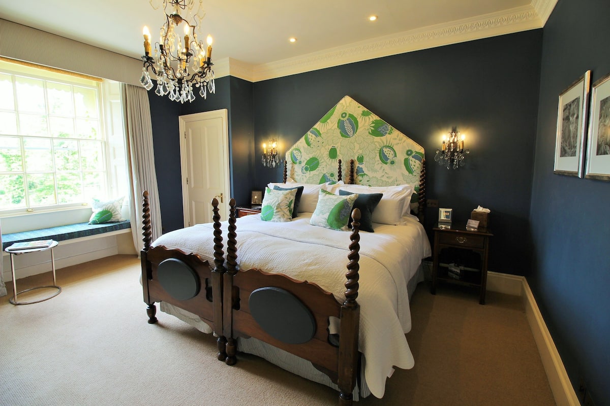 Un dormitorio con una cama grande, un asiento junto a la ventana y un candelabro.