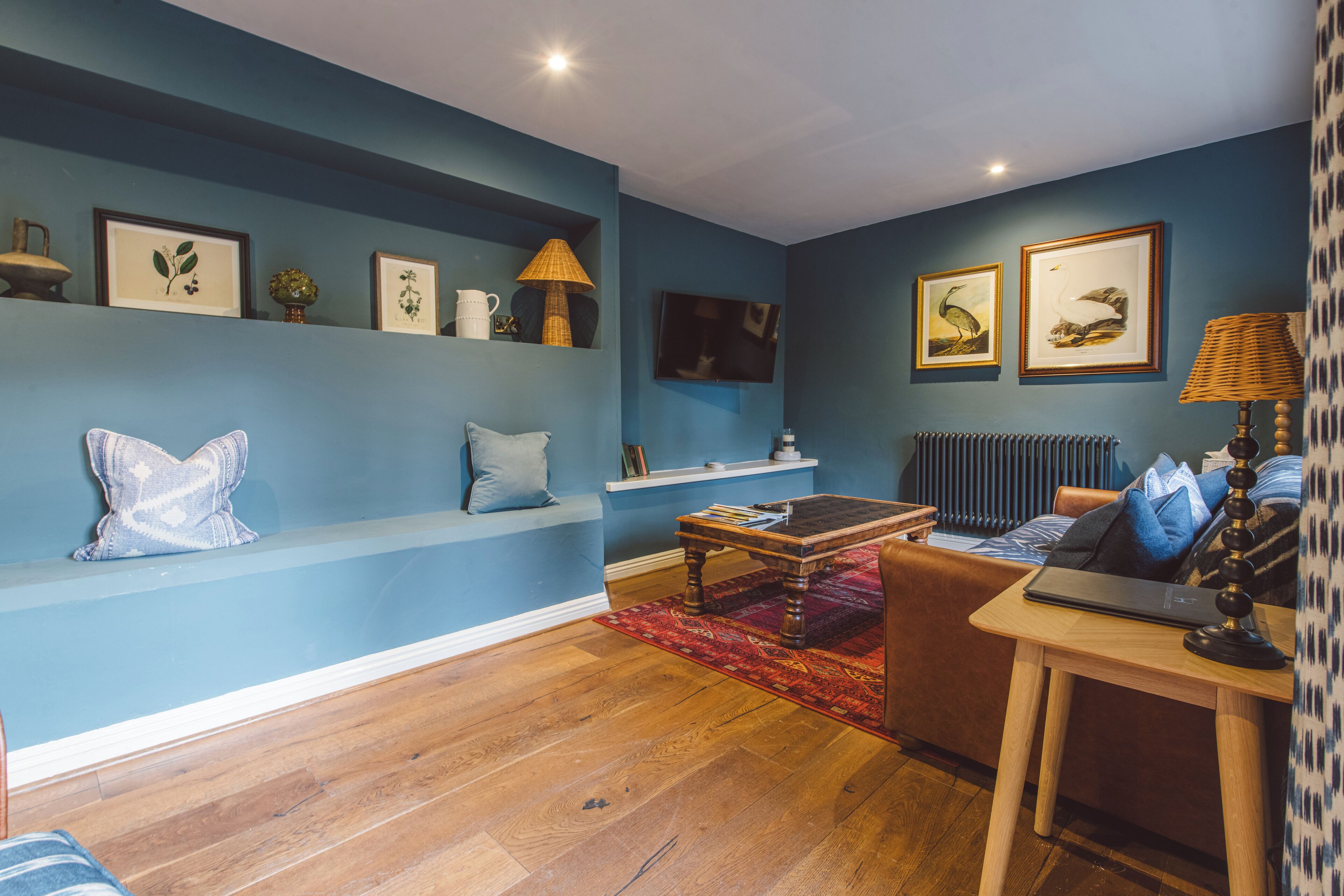 Una sala de estar con una pared azul, piso de madera, un sofá, una mesa de centro y un televisor.