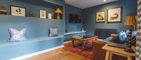 Una sala de estar con una pared azul, piso de madera, un sofá, una mesa de centro y un televisor.
