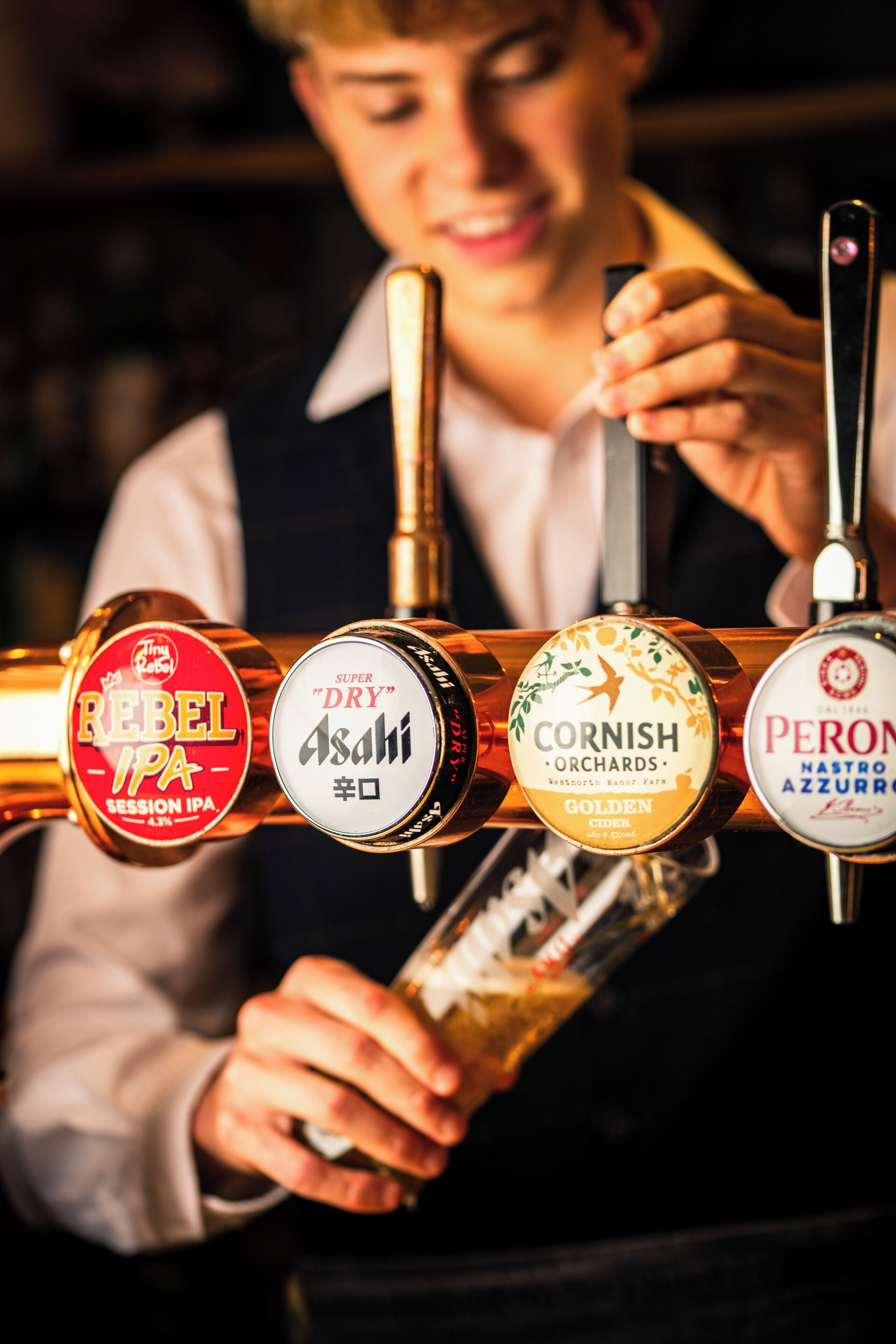 Un barman sostiene una llave de cerveza con diferentes etiquetas.