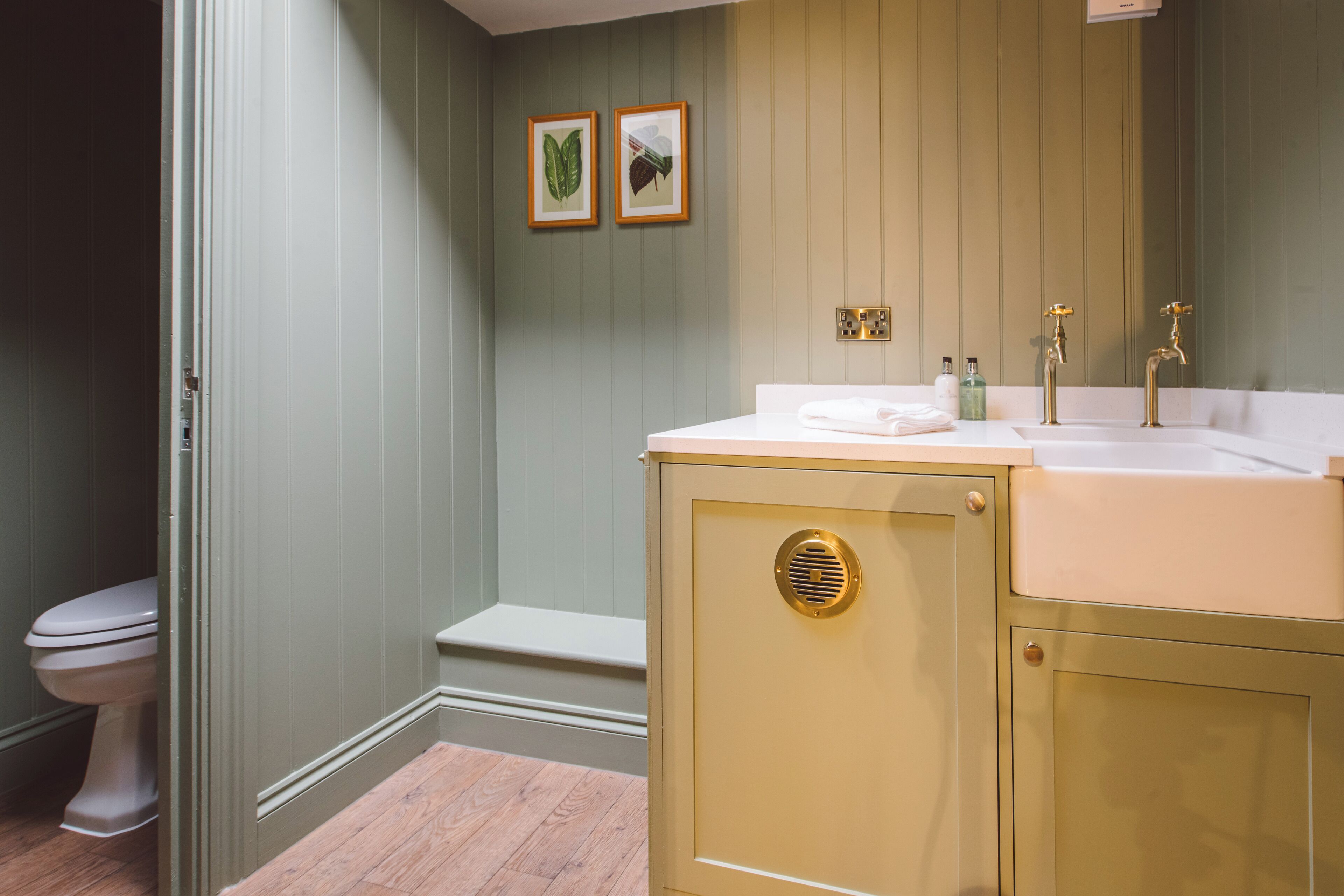 A bathroom with a toilet, a sink with a mirror, and two framed pictures on the wall.