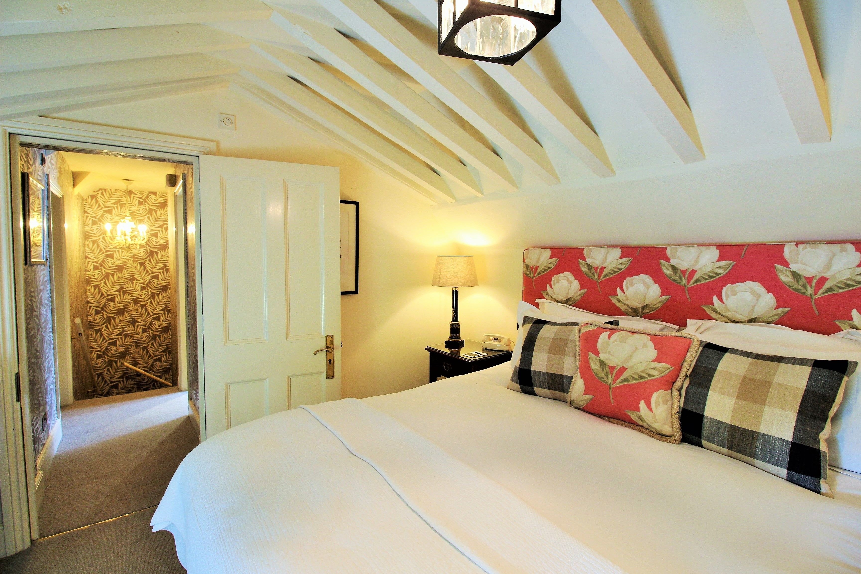 Un dormitorio con cama, mesita de noche, lámpara y puerta que da a un pasillo.