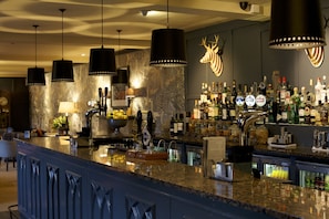 A bar area with a granite countertop, multiple bottles of alcohol, and a deer head decoration on the wall. - Swan Hotel (Cirencester)