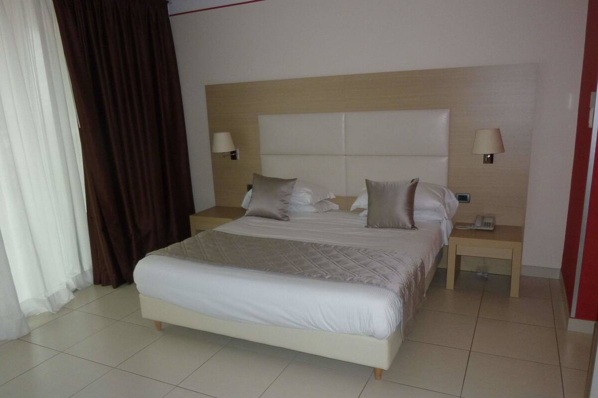 Una habitación de hotel con una cama grande, dos mesitas de noche y un cabecero.