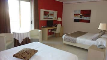 Habitación de hotel con dos camas, un escritorio, una silla, un televisor y obras de arte en las paredes.
