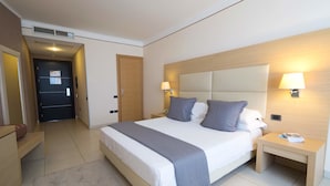 Una habitación de hotel con una cama grande, dos mesitas de noche, una lámpara de pared y una puerta.