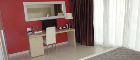 A hotel room with a bed, a desk with a chair, a large mirror, a TV, and a window with curtains.