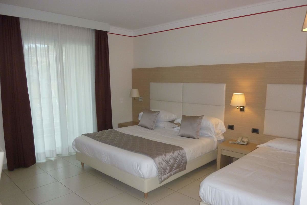 Habitación de hotel con una cama grande, una cama más pequeña, una mesita de noche con teléfono y una ventana con cortinas.